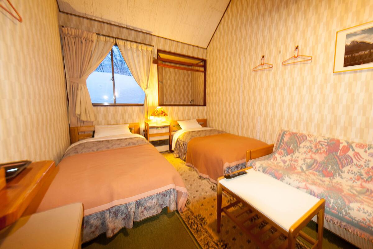 A hotel room with two single beds, a sofa, a small table, and a window with curtains.