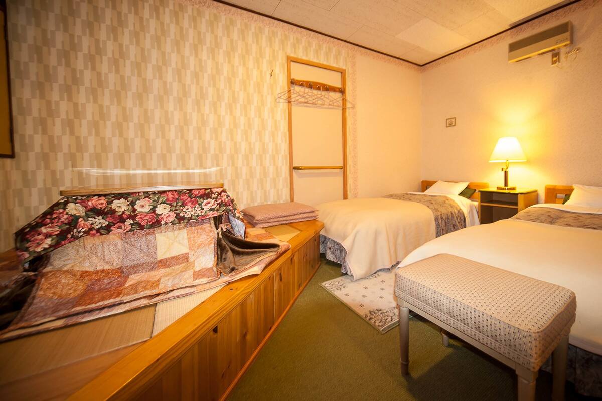 A hotel room with two beds, a wooden desk, a mirror, and a lamp.