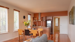 A modern kitchen with wooden cabinets and a stainless steel range hood, a dining area with a wooden table and chairs, and a living room with a grey sofa and a coffee table. - Queensberry Springs Villa 1 (Daylesford)