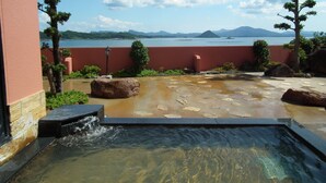 A spa area with a hot spring, surrounded by a red wall, with a view of the sea and mountains in the background. - Hotel Shouryuen Kaisei (Kamiamakusa)