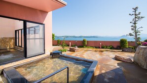 A spa area with a hot tub, a stone wall, and a view of the sea. - Hotel Shouryuen Kaisei (Kamiamakusa)