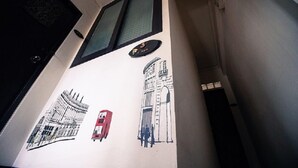 Een gang met een deur, een raam en een muur met een deurbord en een muurschildering van een gebouw en een rode telefooncel.