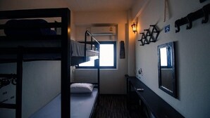 Een slaapzaal met stapelbedden, een raam, een bureau en wandlampen.
