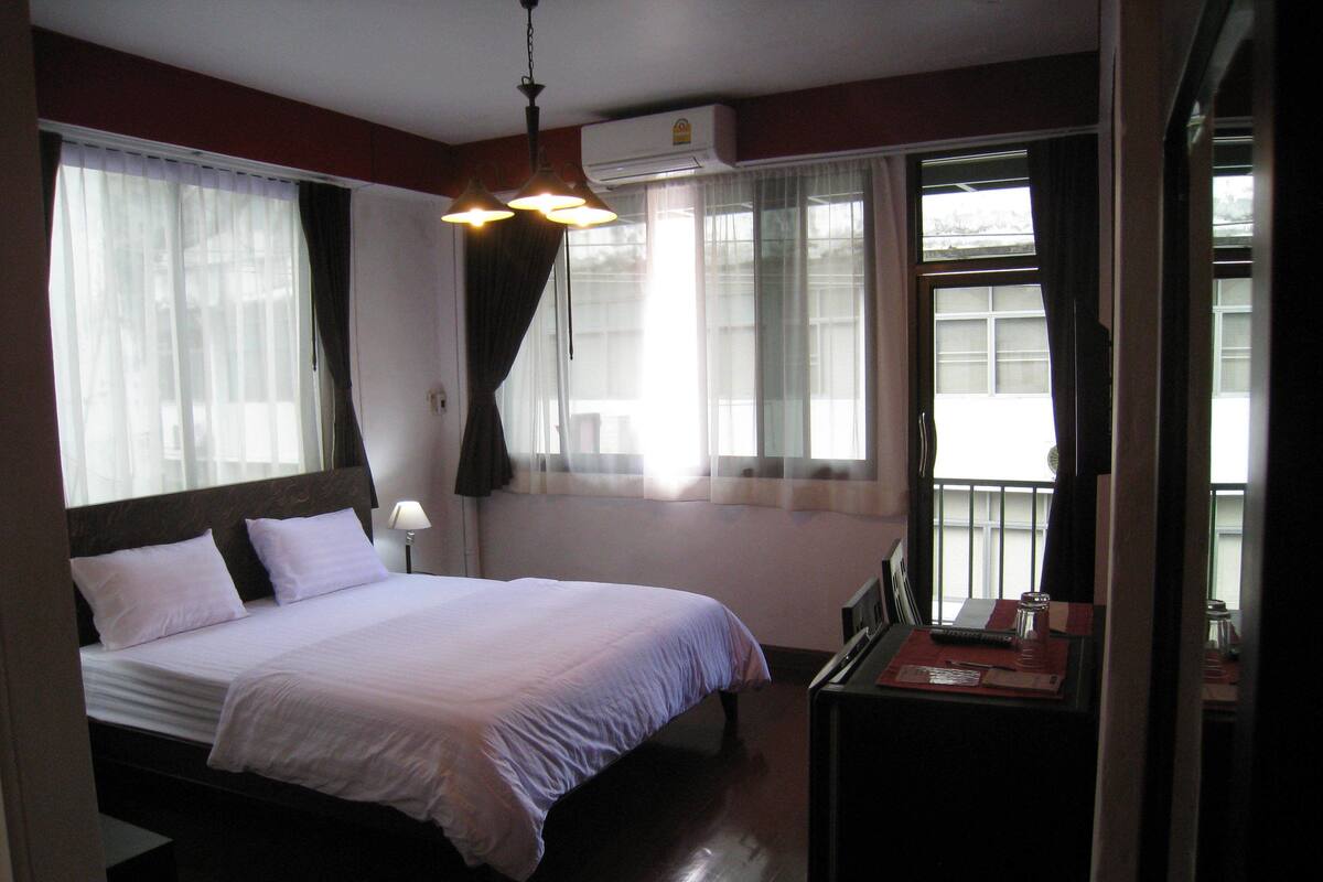 Une chambre d’hôtel avec un lit, un bureau doté d’une lampe et une fenêtre avec des rideaux.