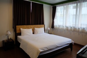 A hotel room with a large bed, two bedside tables with lamps, a headboard, and a window with curtains.
