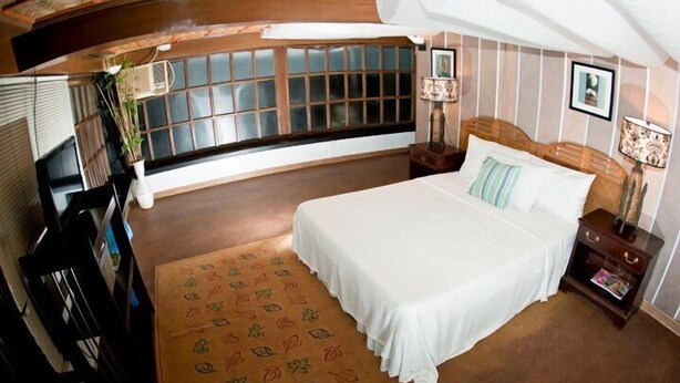 A bedroom with a large bed, a window with blinds, a bedside table with a lamp, and a decorative rug. - Potipot Gateway Resort (Candelaria)