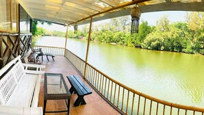 Une terrasse couverte avec vue sur une rivière, des bancs en bois et une table.