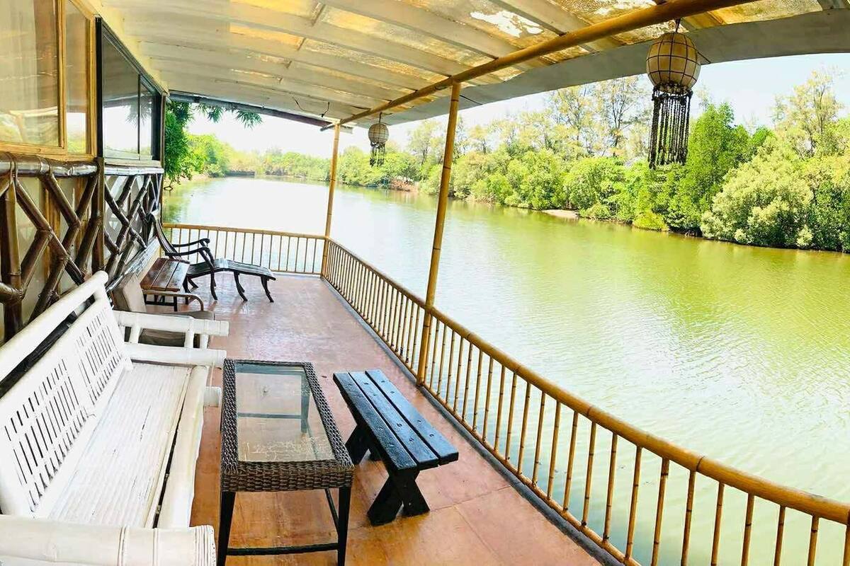 A covered deck with a view of a river, wooden benches, and a table.