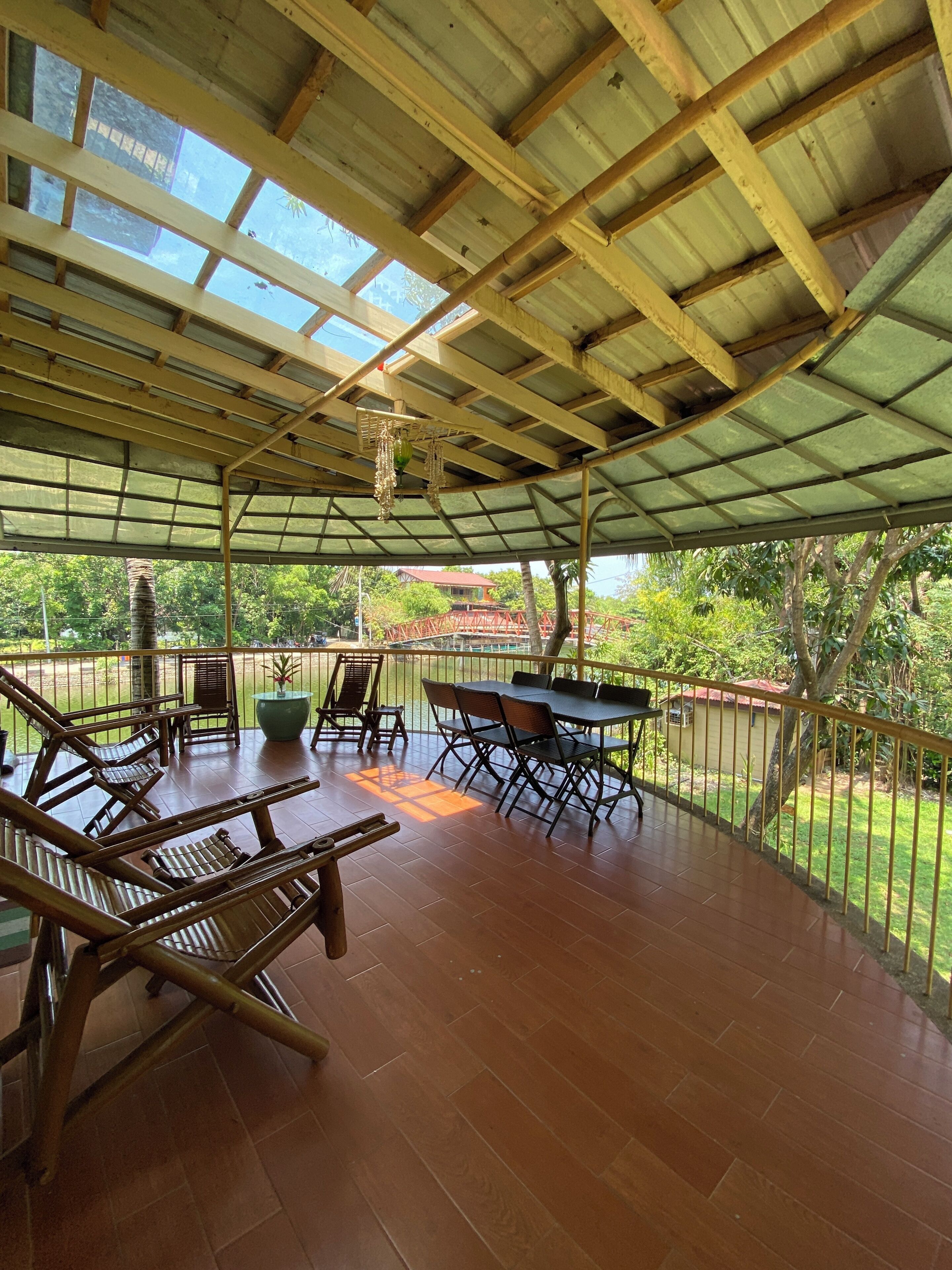 A covered outdoor area with wooden furniture and a table, surrounded by a metal railing.