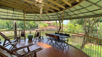 A covered outdoor area with wooden furniture and a table, surrounded by a metal railing.