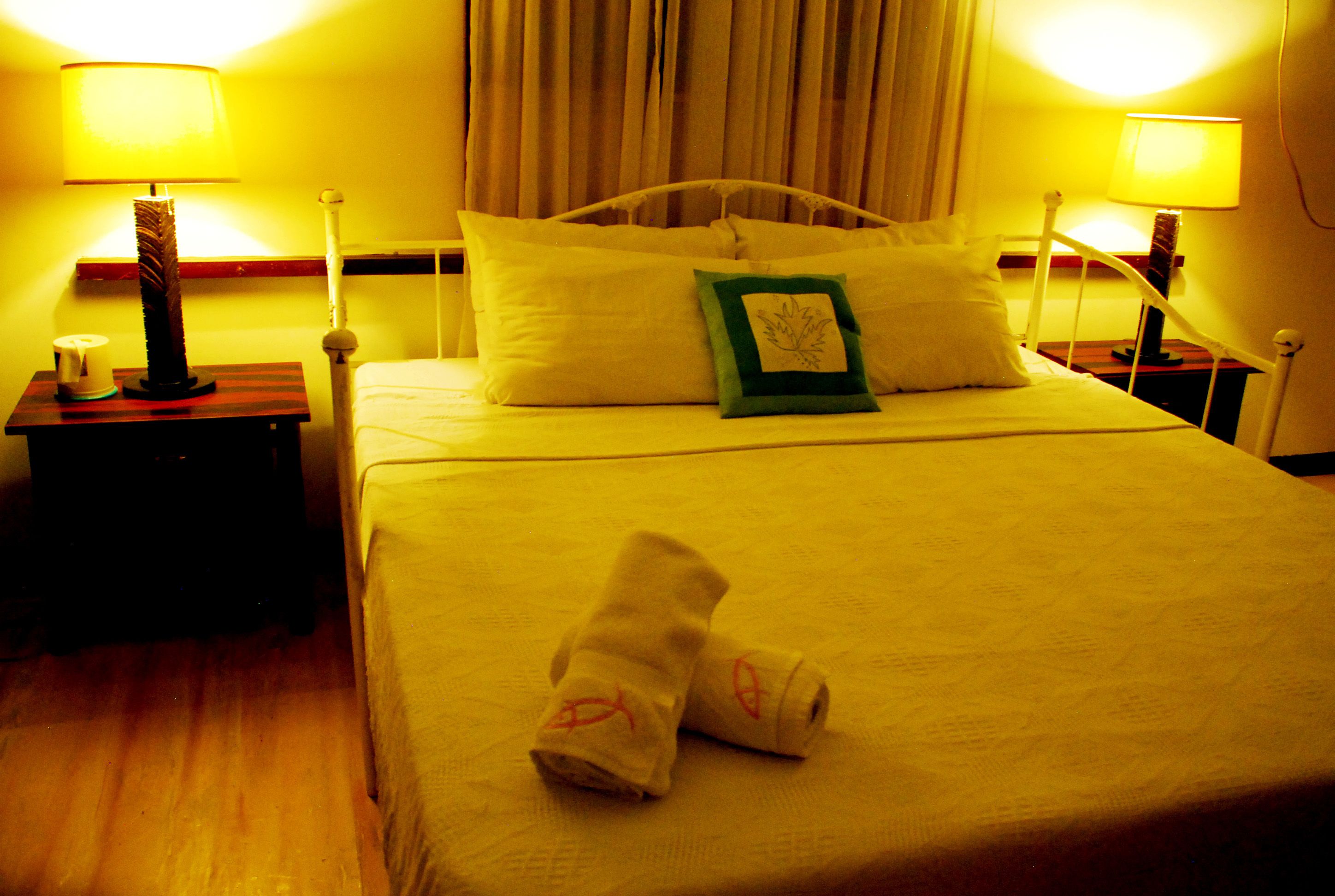 A hotel room with a bed, two bedside tables, lamps, and a pair of towels on the bed.