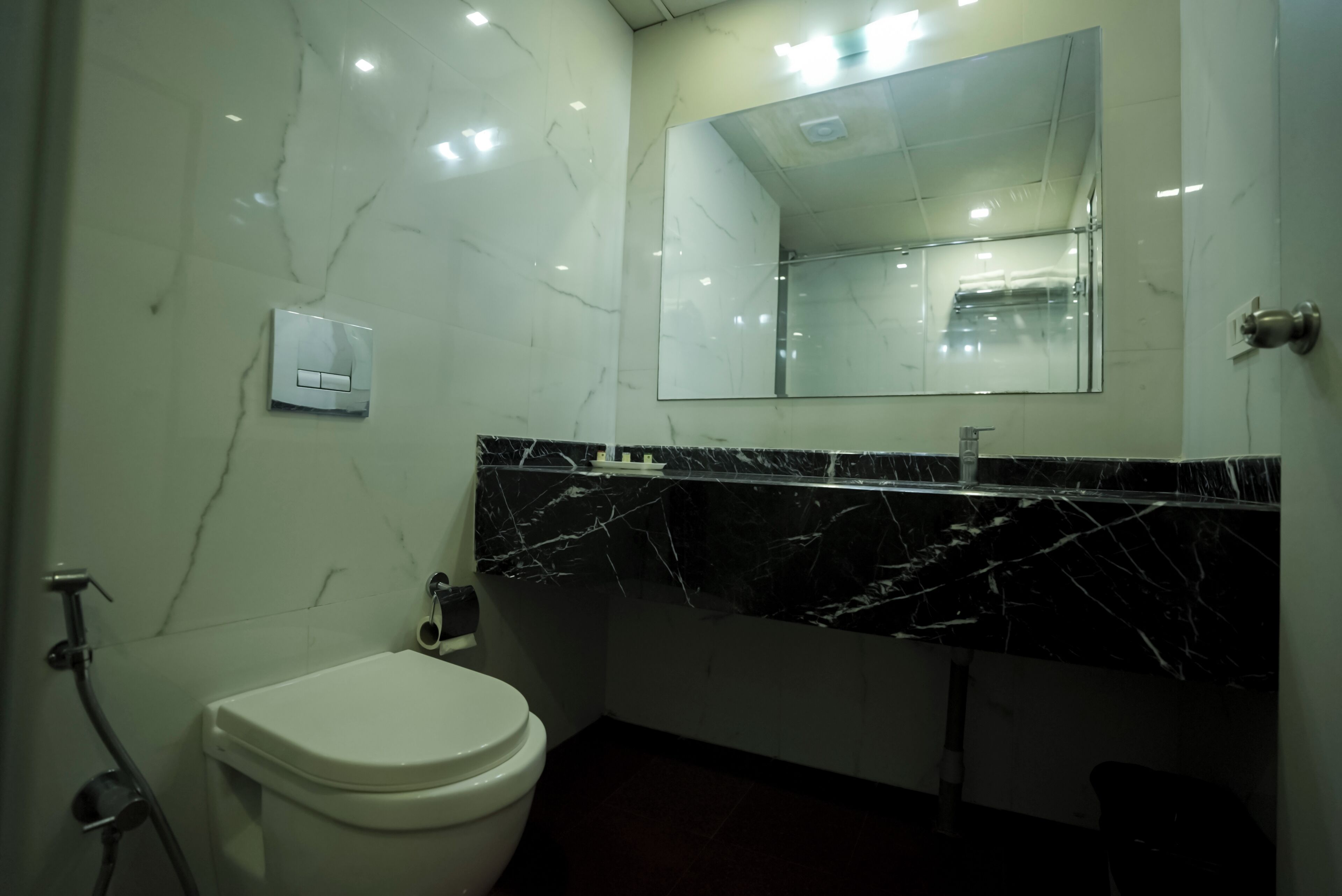Ein Badezimmer mit einer weißen Toilette, einem schwarzen Marmorwaschbecken und einem großen Spiegel darüber.
