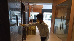 Una persona con camisa y guantes extendiendo la mano hacia una puerta de cristal.