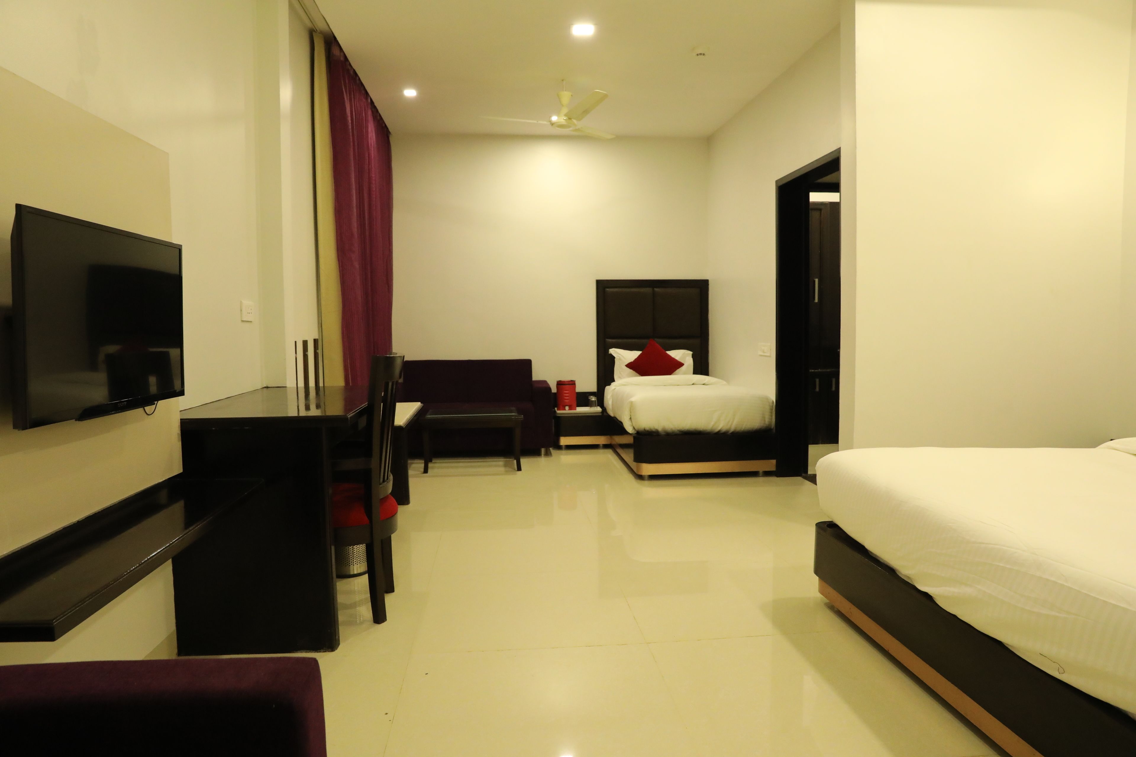 A modern hotel room with a flat-screen TV, a bed with white bedding, a desk with a chair, and a ceiling fan.