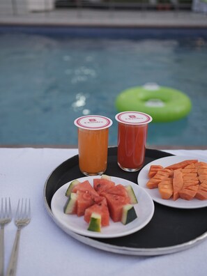 Una bandeja con rebanadas de sandía, dos bebidas y un flotador verde junto a una piscina.