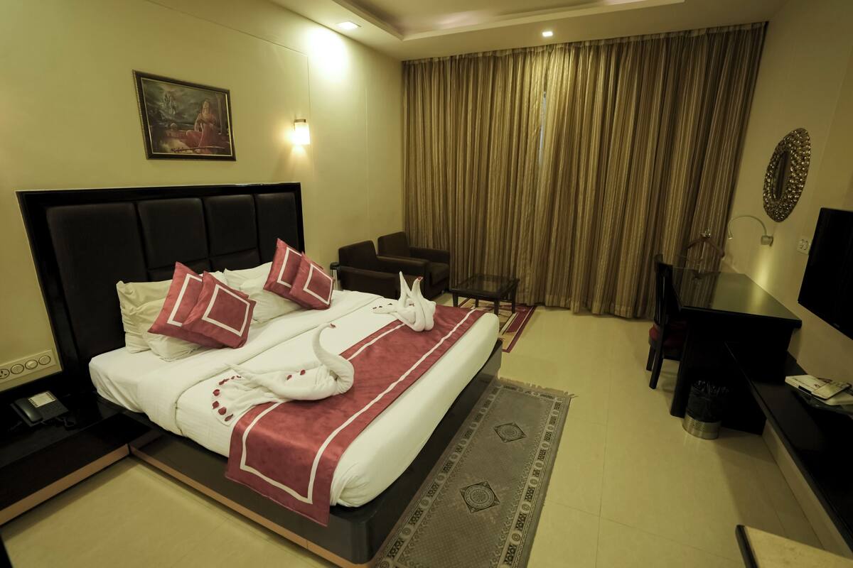 Ein Hotelzimmer mit einem großen Bett, einem Schreibtisch, einem Sessel, einem Fernseher und einem Gemälde an der Wand.