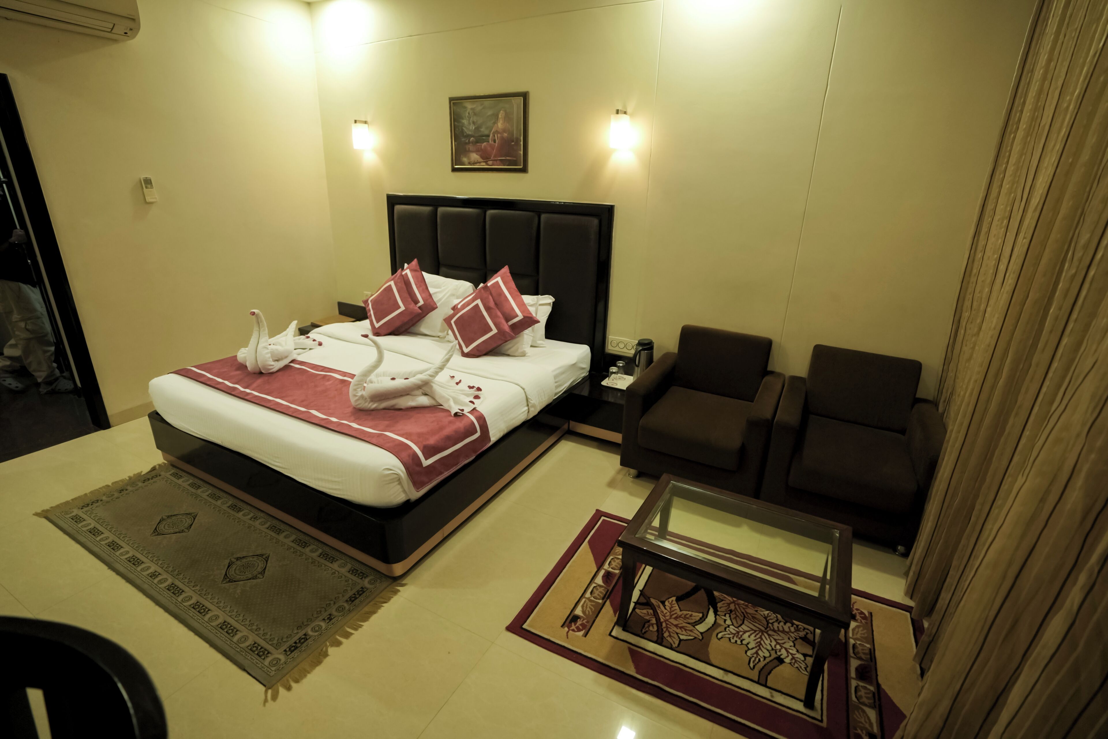 A hotel room with a bed, two armchairs, a coffee table, and a painting on the wall.