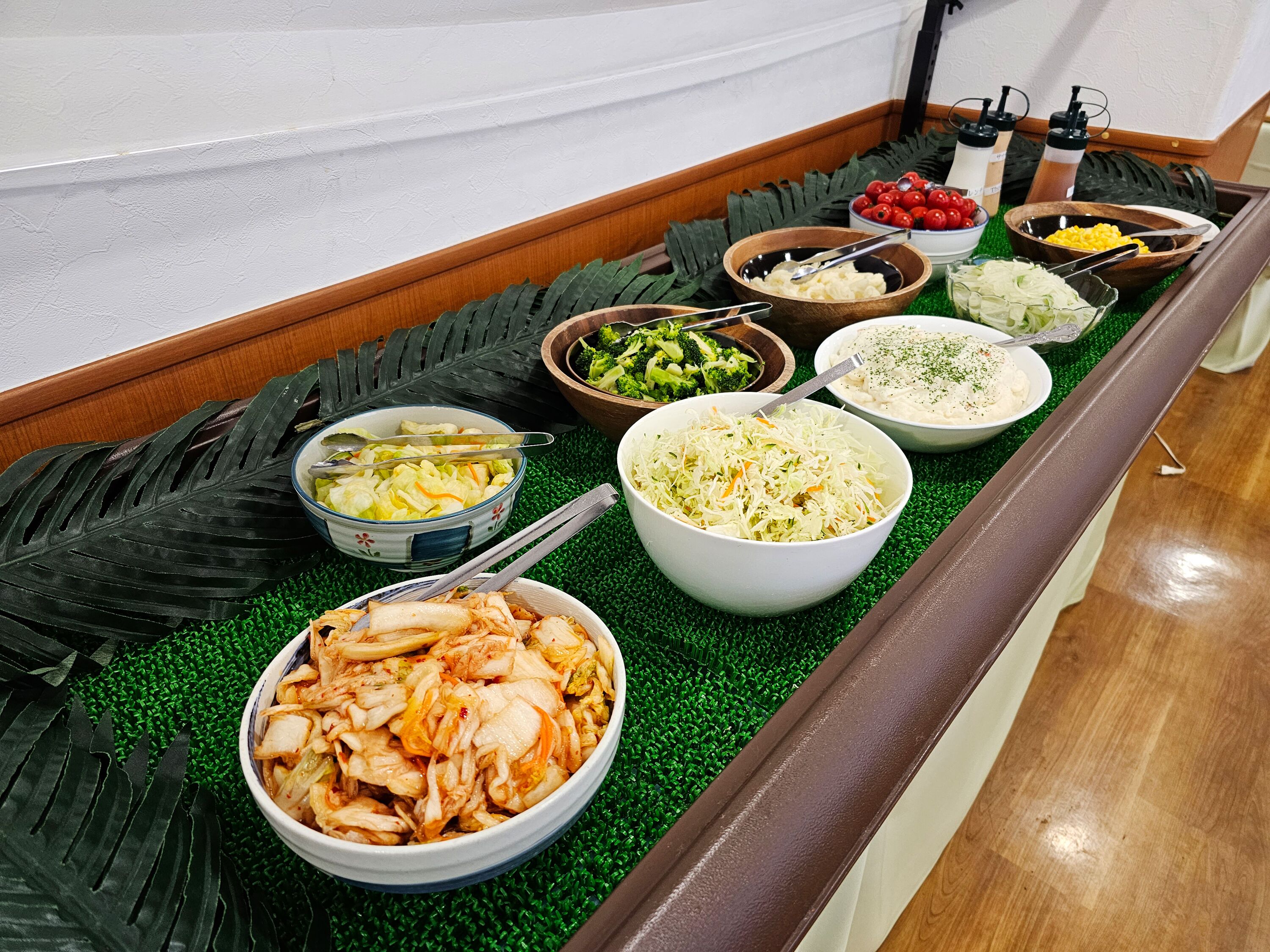 A buffet table with various dishes including kimchi, coleslaw, and a bowl of corn.