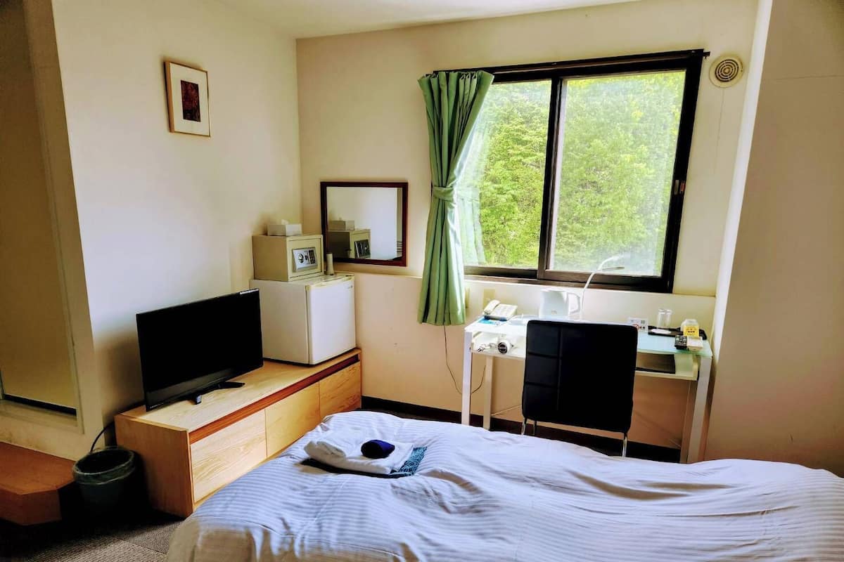 Ein Hotelzimmer mit einem Bett, einem Schreibtisch mit Computer, einem Fernseher und einem Fenster mit Vorhängen.