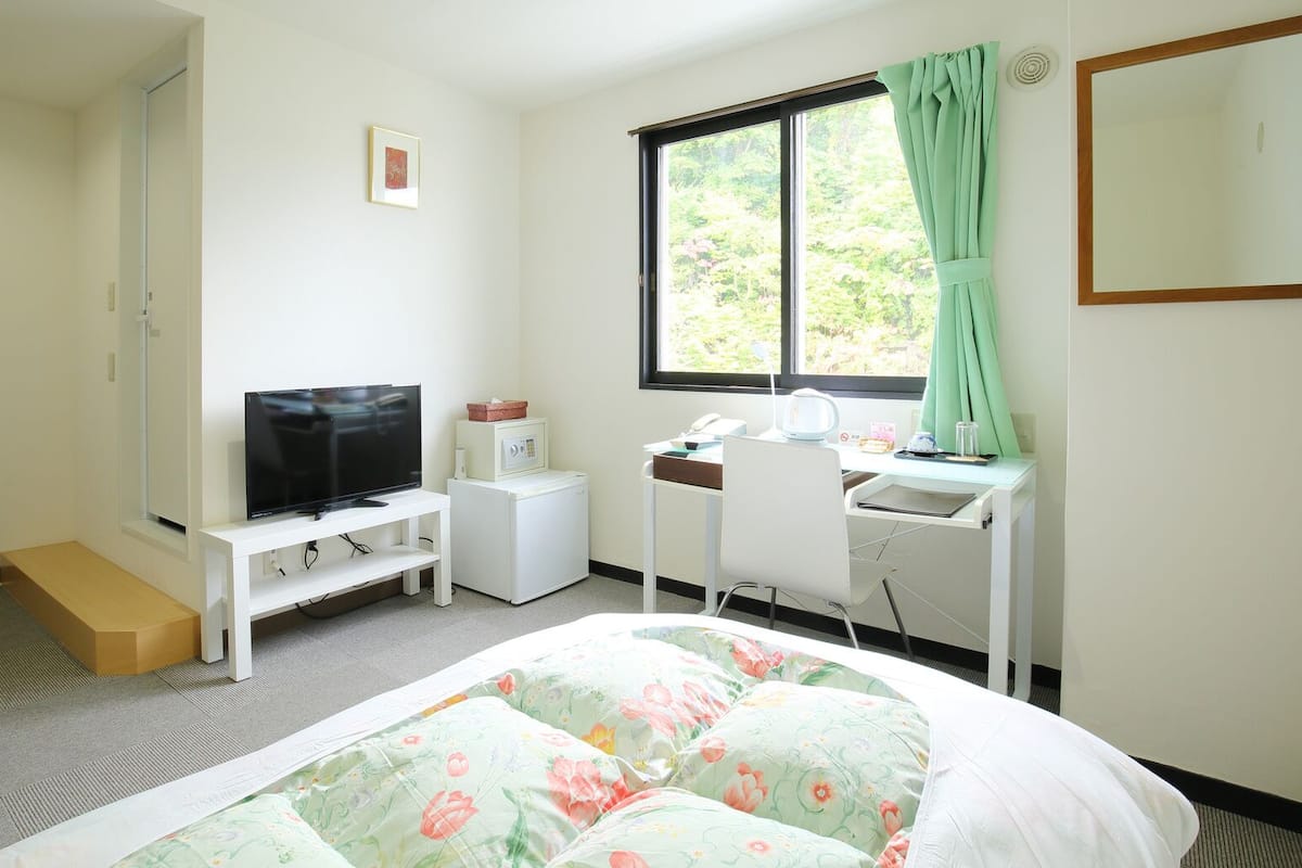 Une chambre d’hôtel comprenant un lit, un bureau avec une chaise, une télévision, un lave-linge et une fenêtre avec des rideaux.