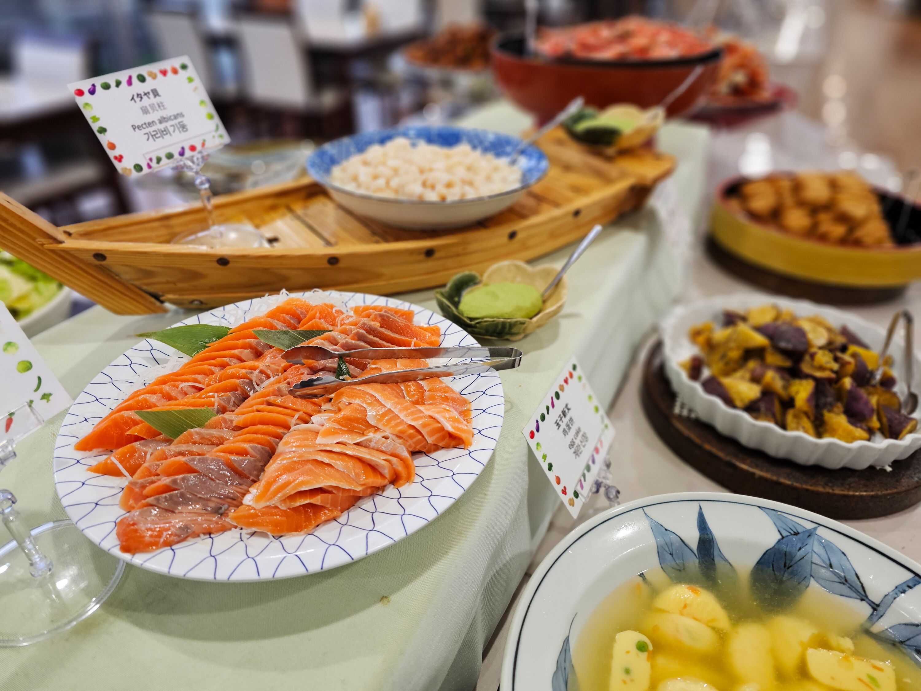 Una mesa de bufé con diversos platos, incluyendo salmón, verduras y un tazón de sopa.