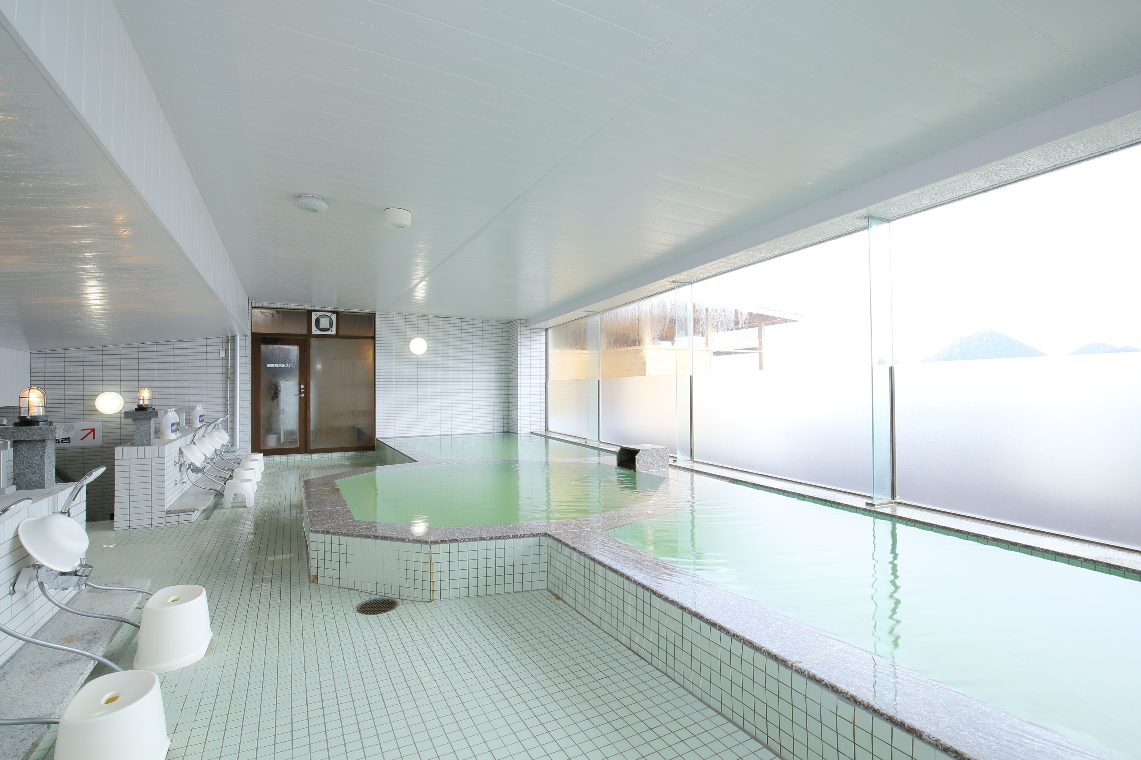 A modern indoor swimming pool with a view of mountains, tiled walls, and a row of sinks.