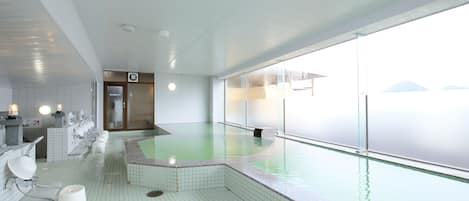 Una piscina interior moderna con vistas a montañas, paredes de azulejos y una fila de lavamanos.