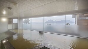 Un extenso baño termal interior con vistas a un paisaje montañoso a través de amplios ventanales.