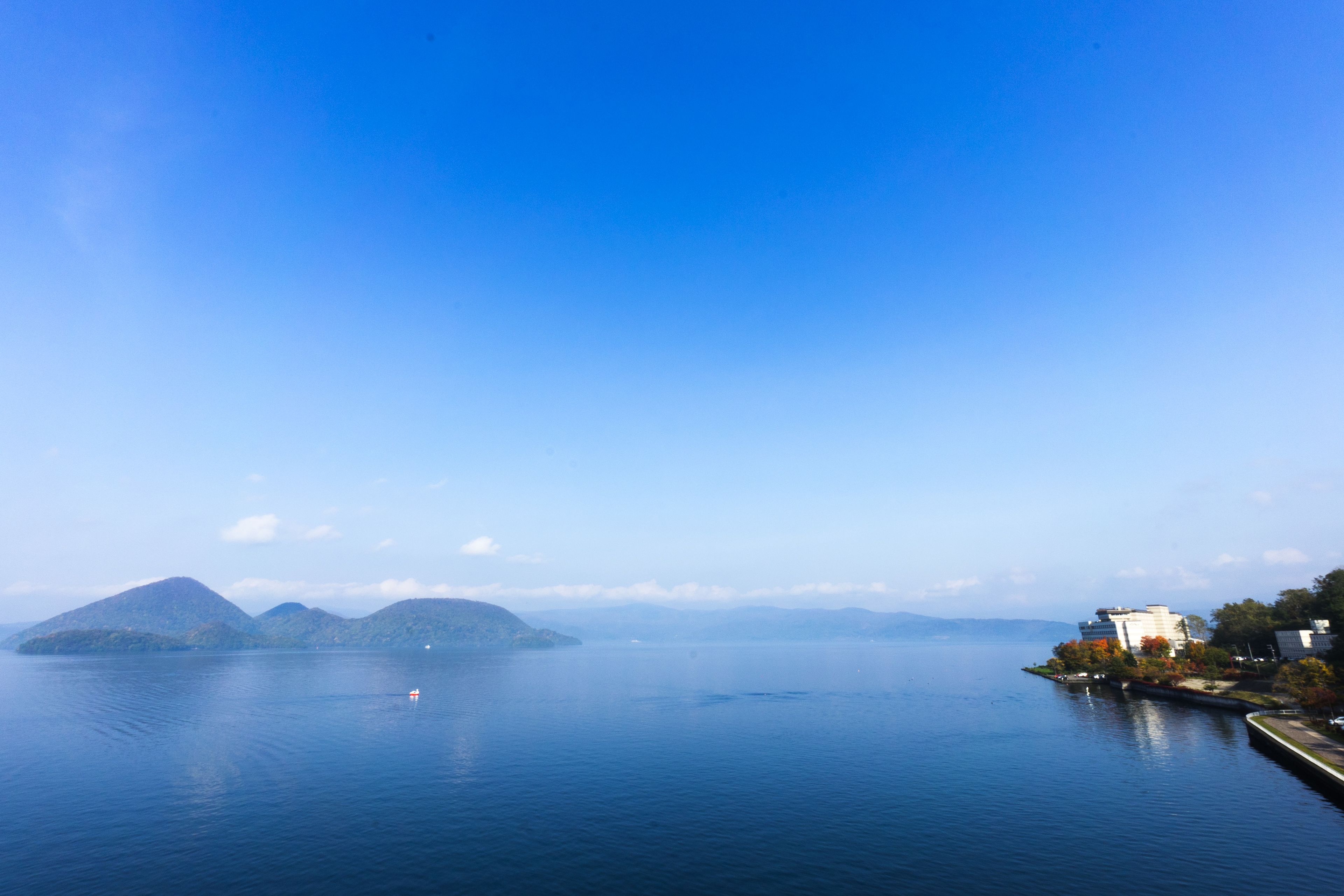 Un lago tranquilo con montañas al fondo y un pequeño edificio a la derecha.