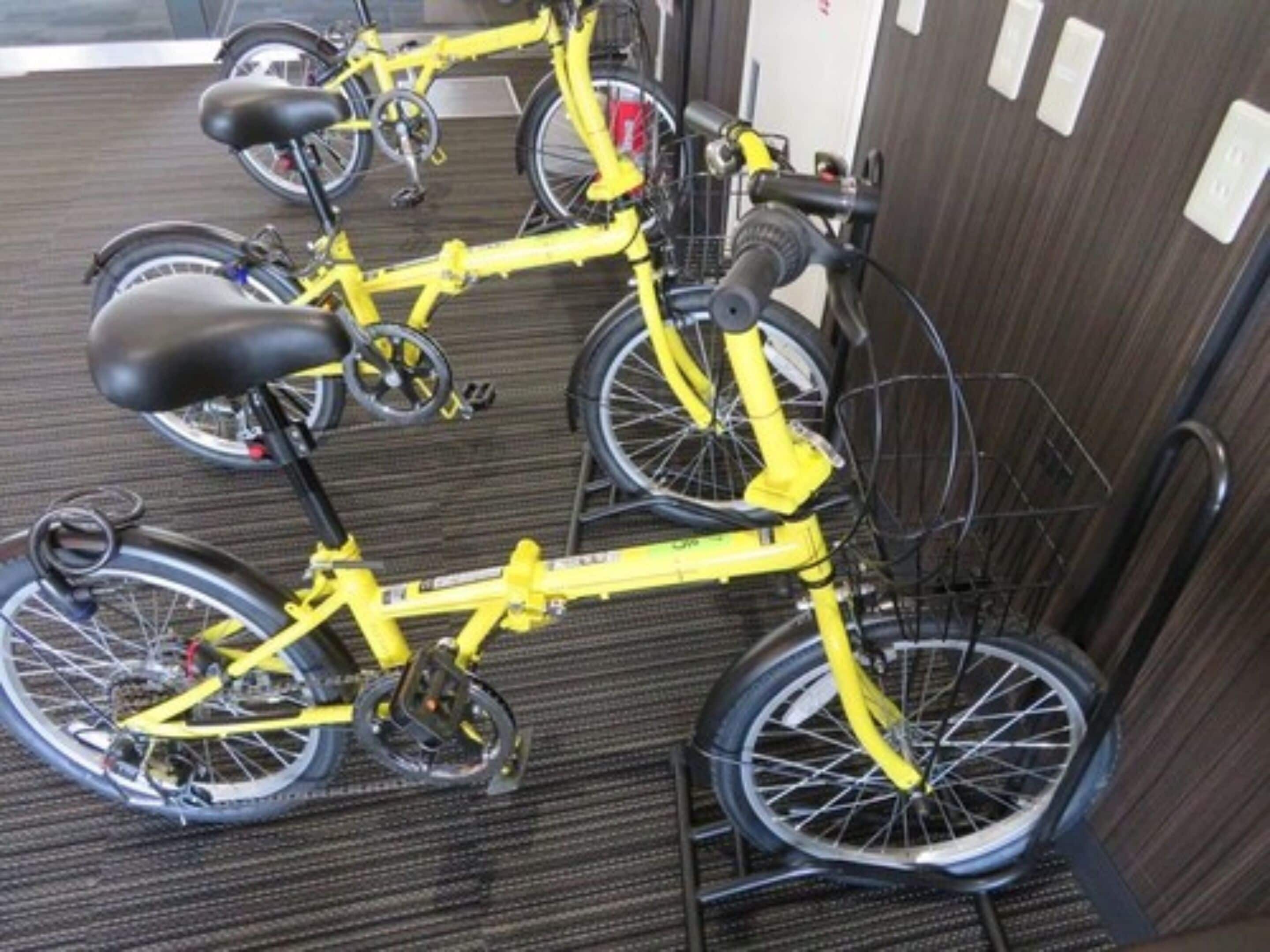 Una bicicleta amarilla con cesta, estacionada en un espacio interior con suelo alfombrado y pared de madera al fondo.