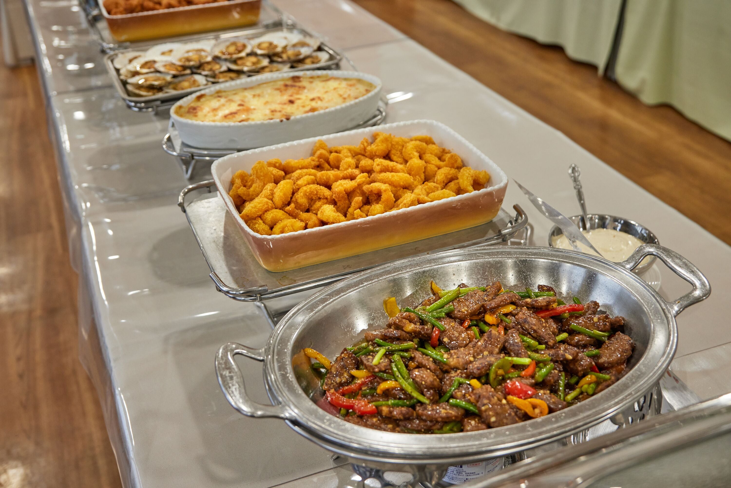 Een buffettafel met diverse gerechten, waaronder een roerbakgerecht met rundvlees, krokante kippnuggets en een ovenschotel.