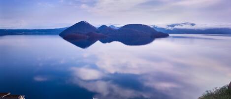 A view of a calm lake with mountains in the distance and a building with multiple floors in the foreground.