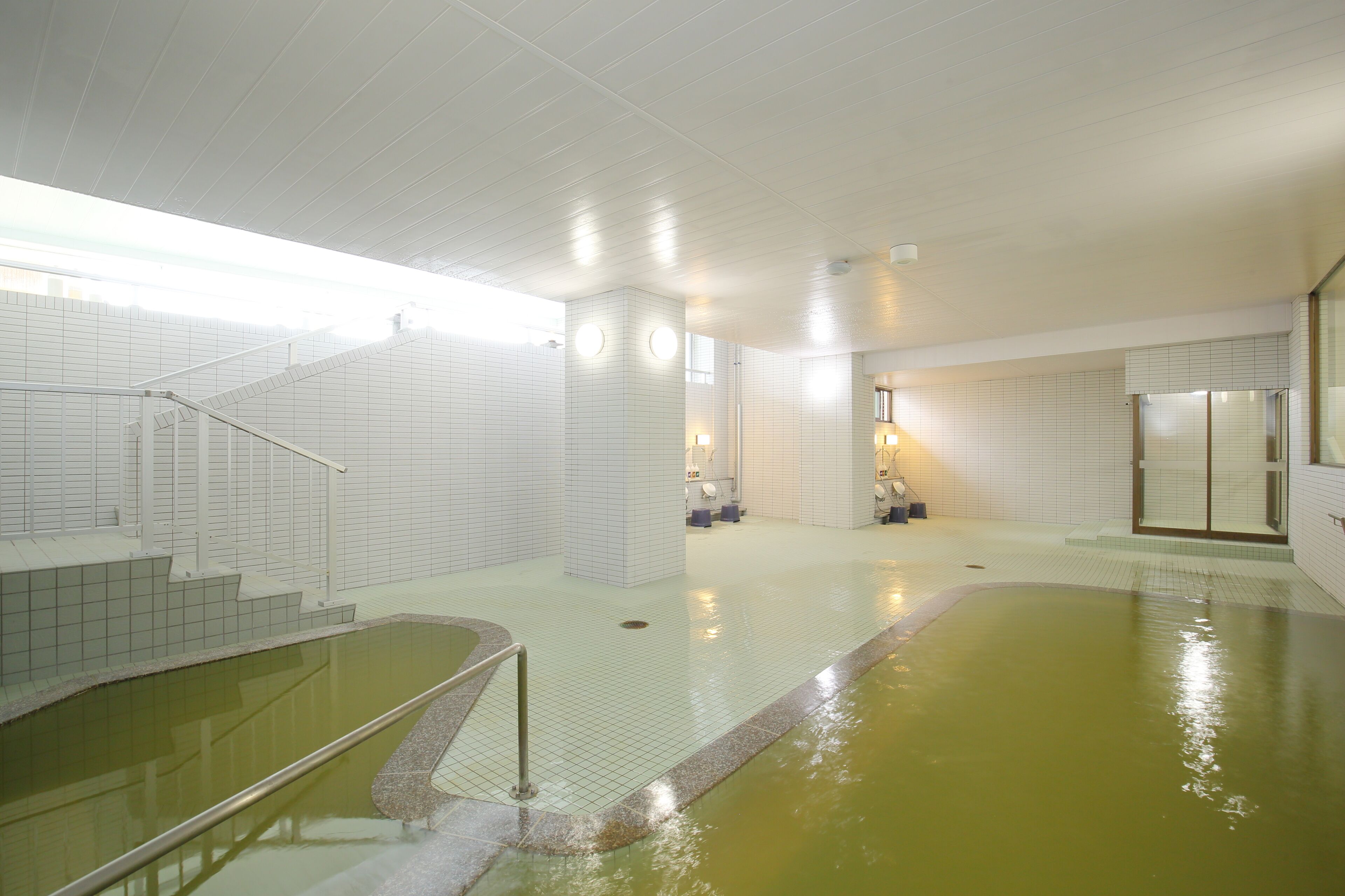 A swimming pool area with tiled walls, a staircase, and a glass door leading to another room.
