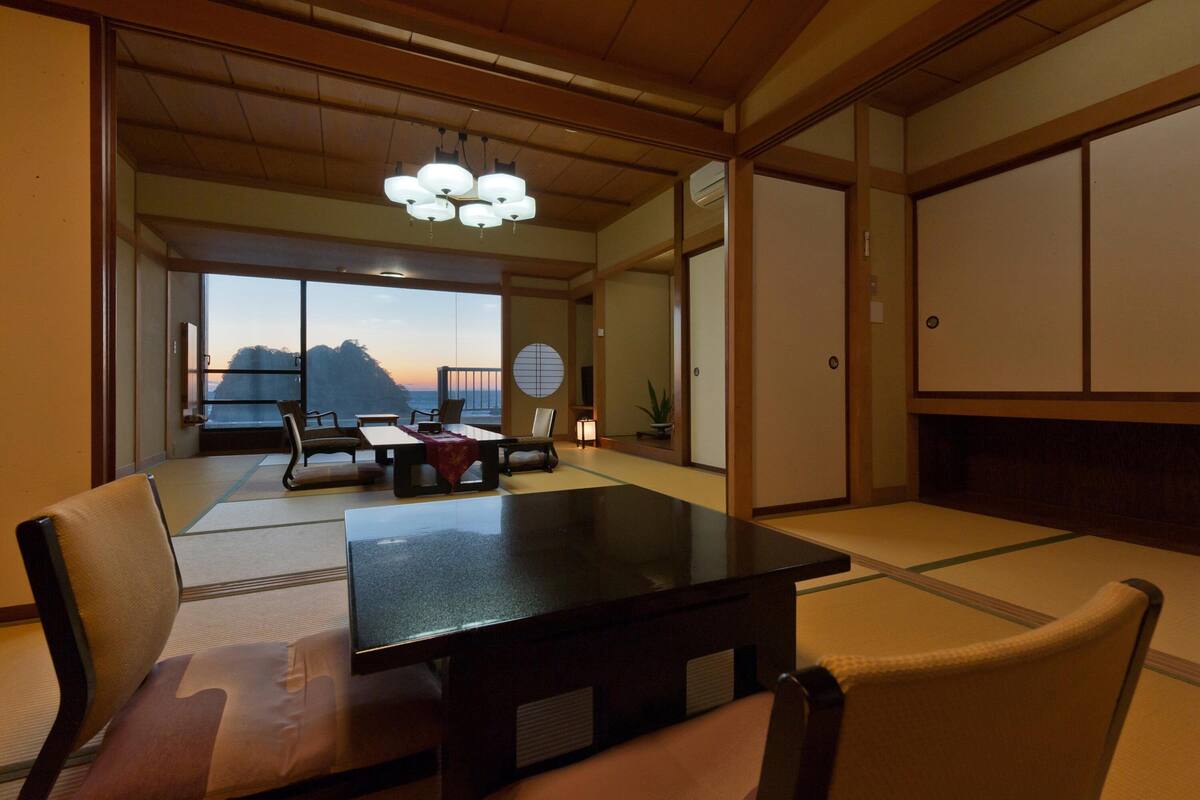 Una habitación japonesa tradicional con suelo de tatami, una mesa baja y vistas a una montaña al atardecer.