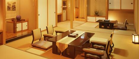 Una habitación japonesa tradicional con suelo de tatami, una mesa baja con cojines y puertas correderas.