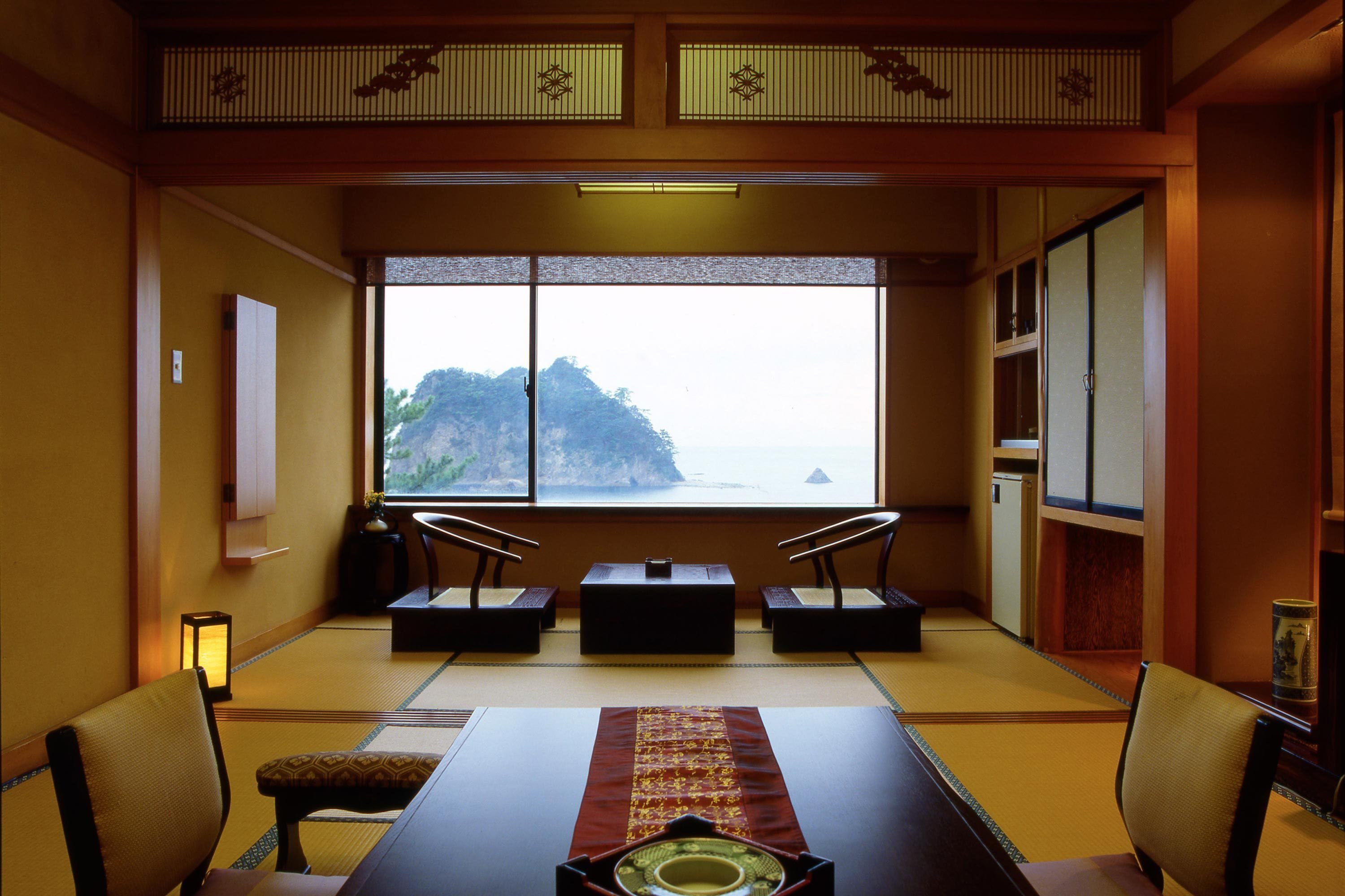 A traditional Japanese room with tatami flooring, a low table with a placemat, and a view of a mountainous landscape through large windows.