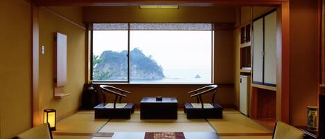 A traditional Japanese room with tatami flooring, a low table with a placemat, and a view of a mountainous landscape through large windows.