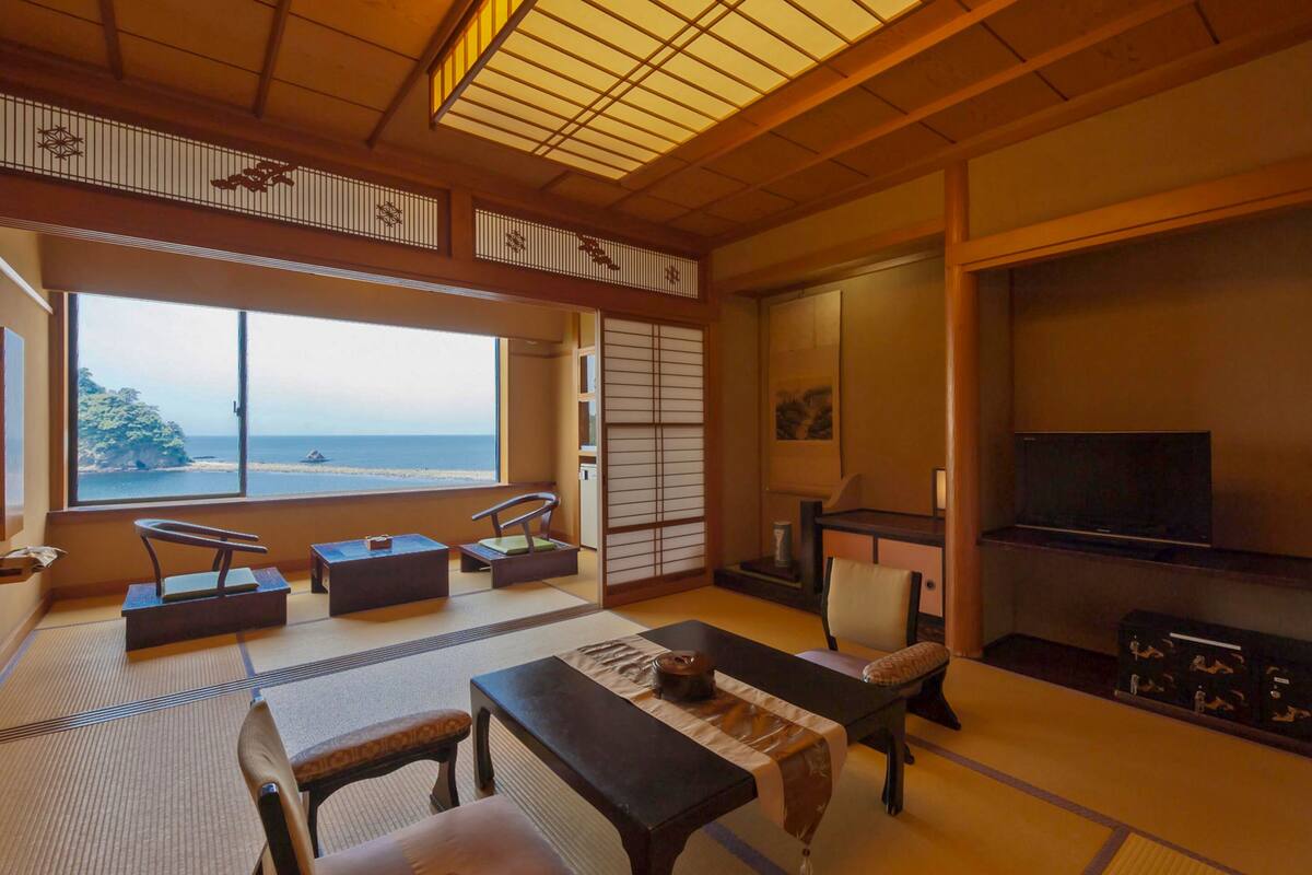Una habitación tradicional japonesa con suelo de tatami, una mesa baja con cojines, un televisor y vistas al mar.