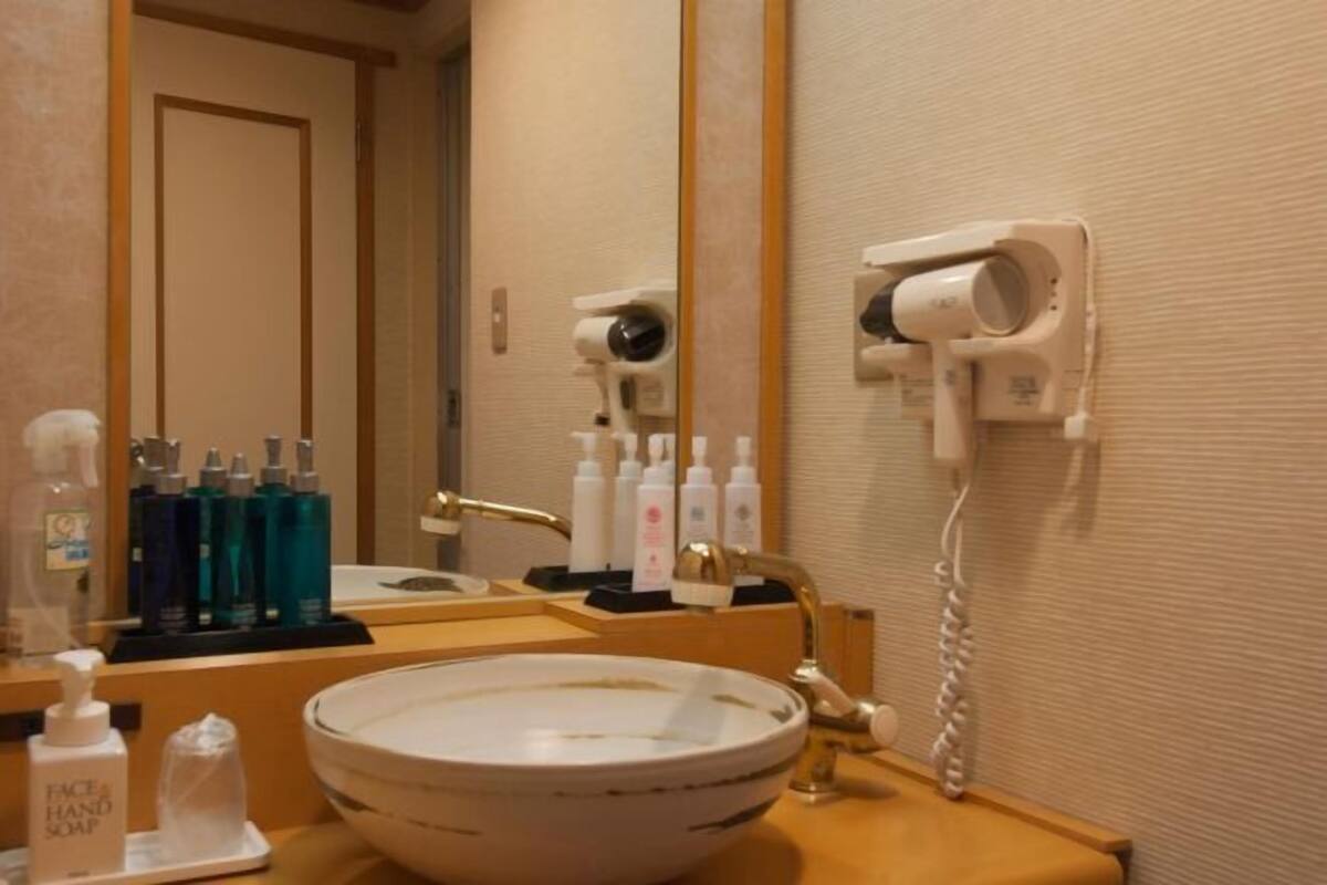 Un baño con un lavamanos grande, un espejo, un secador de pelo y varios artículos de aseo.