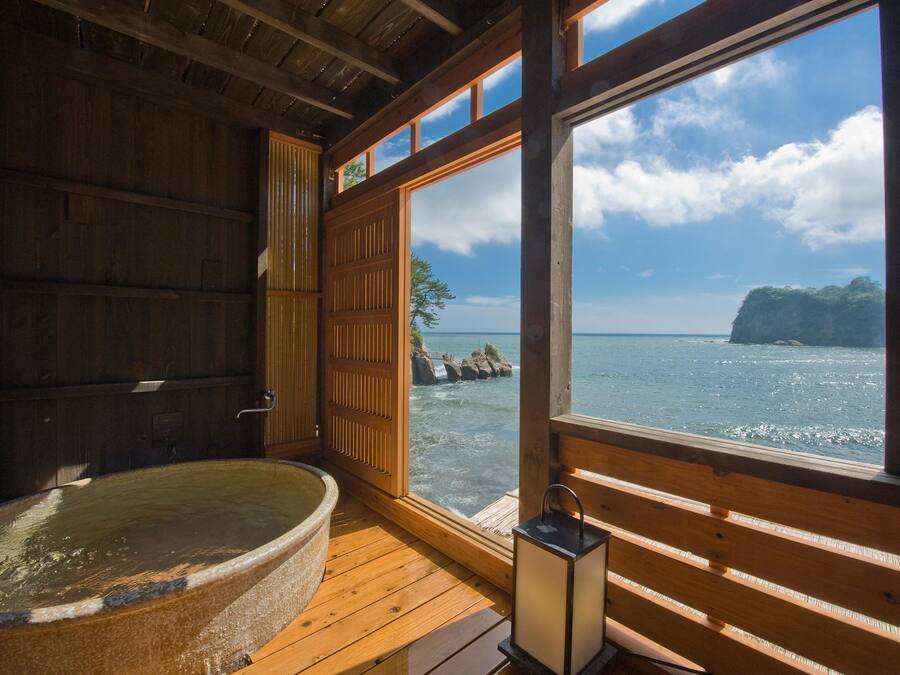A wooden cabin with a large window overlooking a body of water and a rocky island.