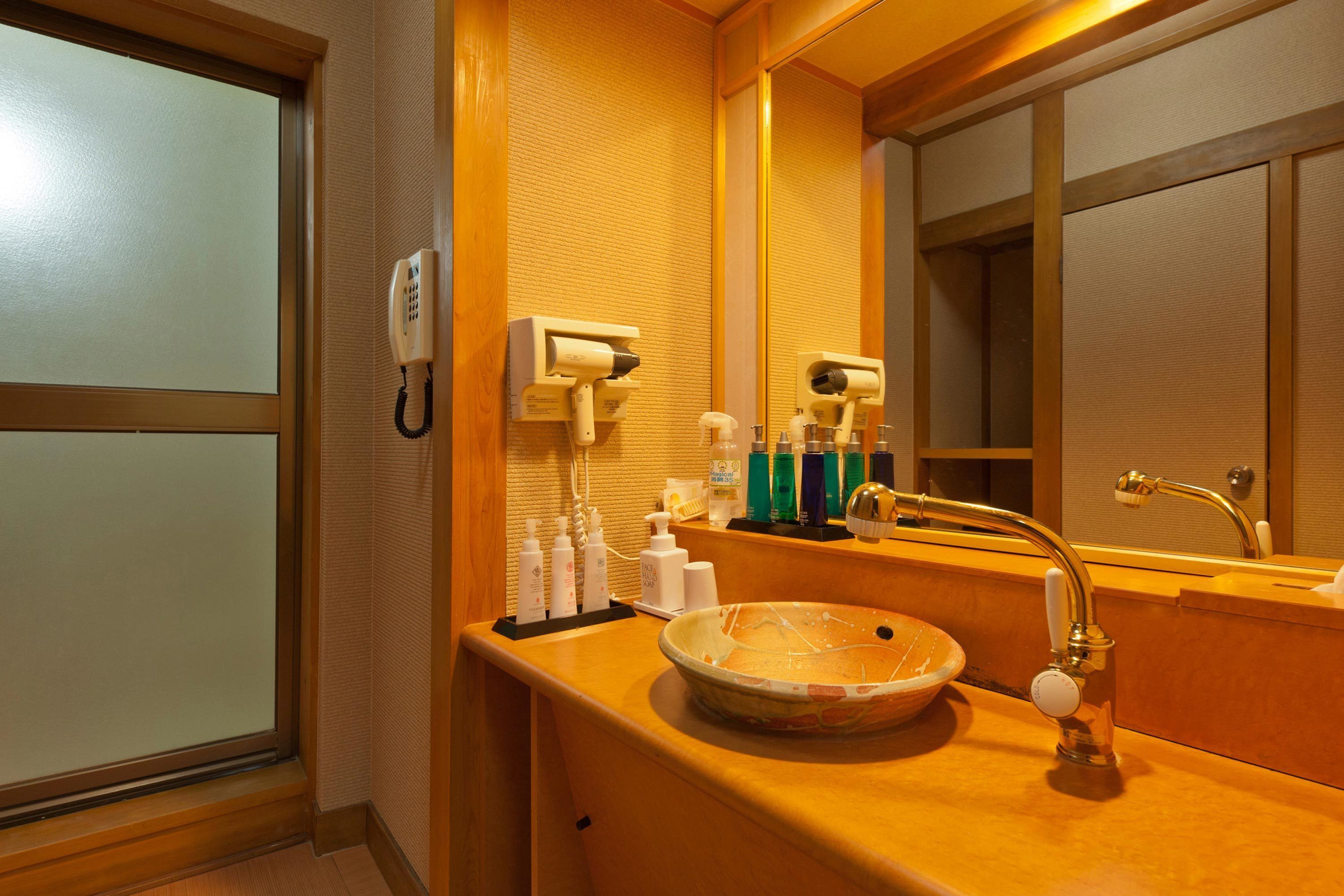 Ein Badezimmer mit einem Holzkosmetikschrank, einem runden Waschbecken, einem Spiegel, einem Telefon und Toilettenartikeln.
