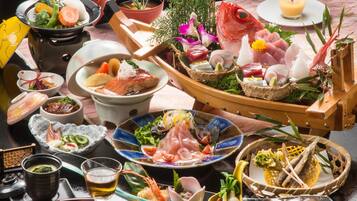 A variety of dishes and drinks on a table, including sushi, sashimi, and a bowl of soup.