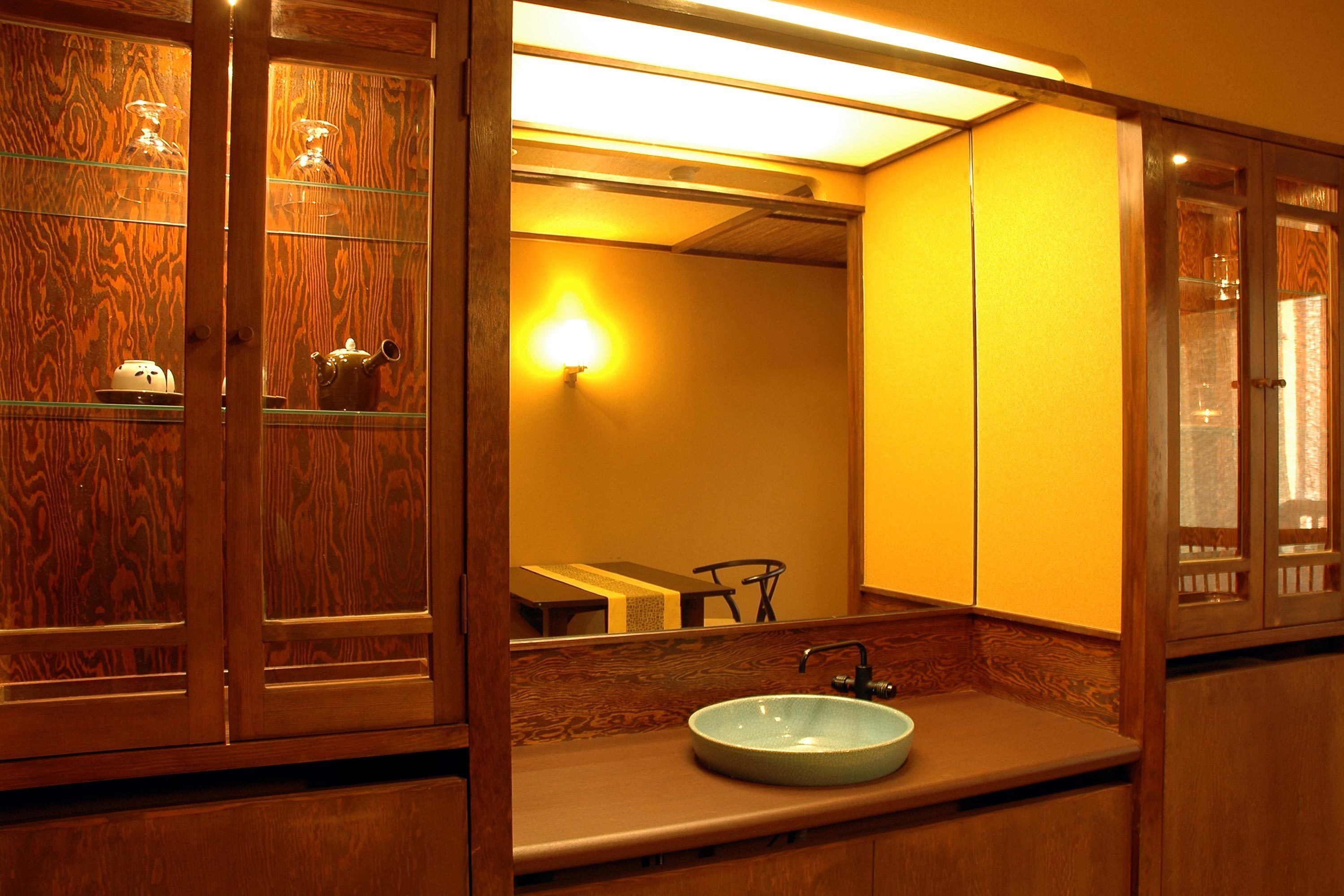 A bathroom with a wooden vanity, a glass shelf with tea sets, and a mirror reflecting the room.