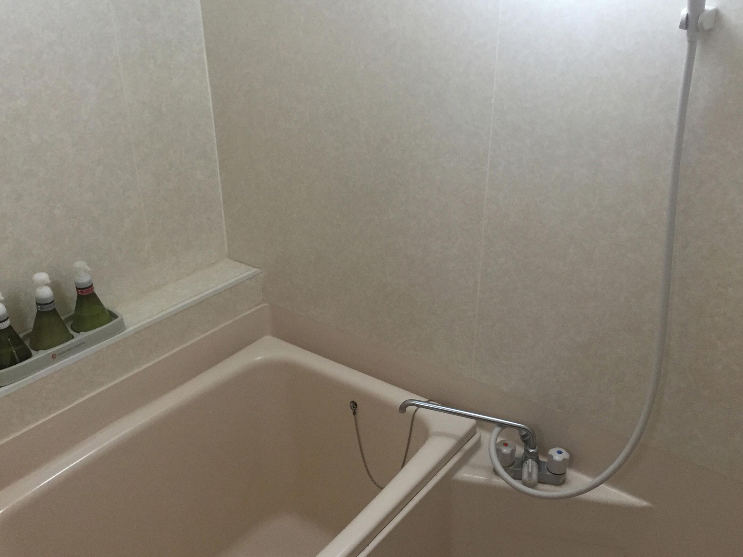 A bathroom with a bathtub, a shower, and a shelf with bottles.