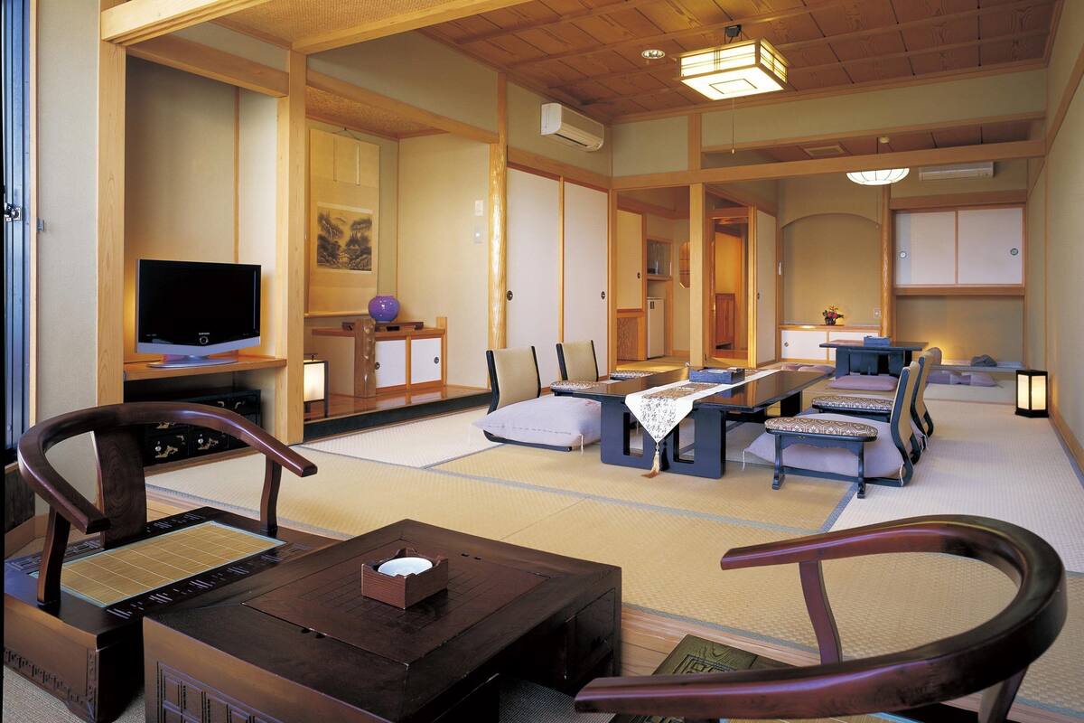 Un salón japonés tradicional con suelo de tatami, un televisor y una baja mesa de madera con una caja encima.