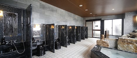 A modern bathroom with multiple shower stalls, a large mirror, and a seating area with a water feature.