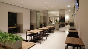 A modern dining area with wooden tables and chairs, a glass partition, and a reception desk with a sign. - Hotel Dormy Inn Miyazaki Natural Hot Spring (Miyazaki)