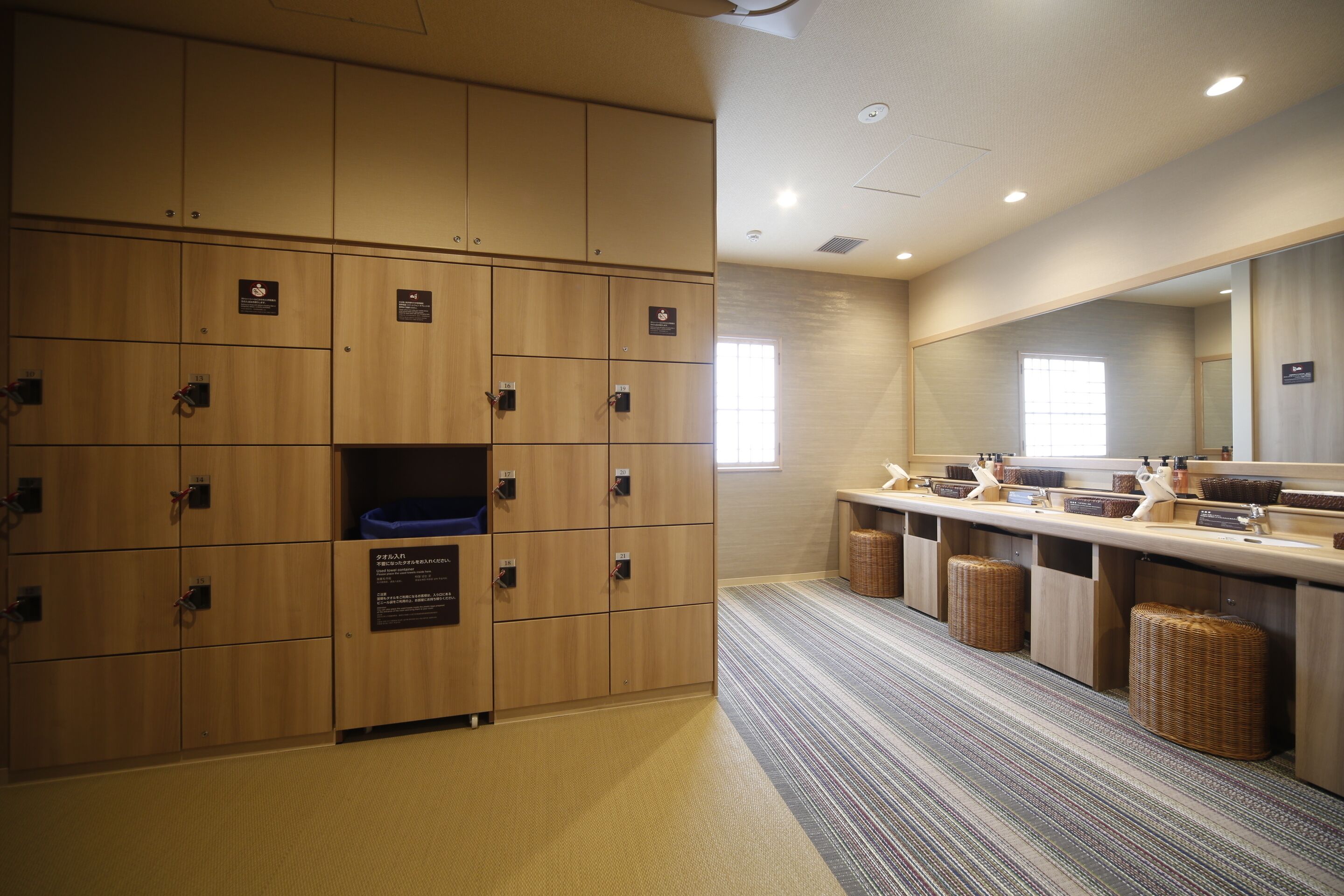 A hotel room with wooden lockers, a long counter with baskets, and a large mirror.
