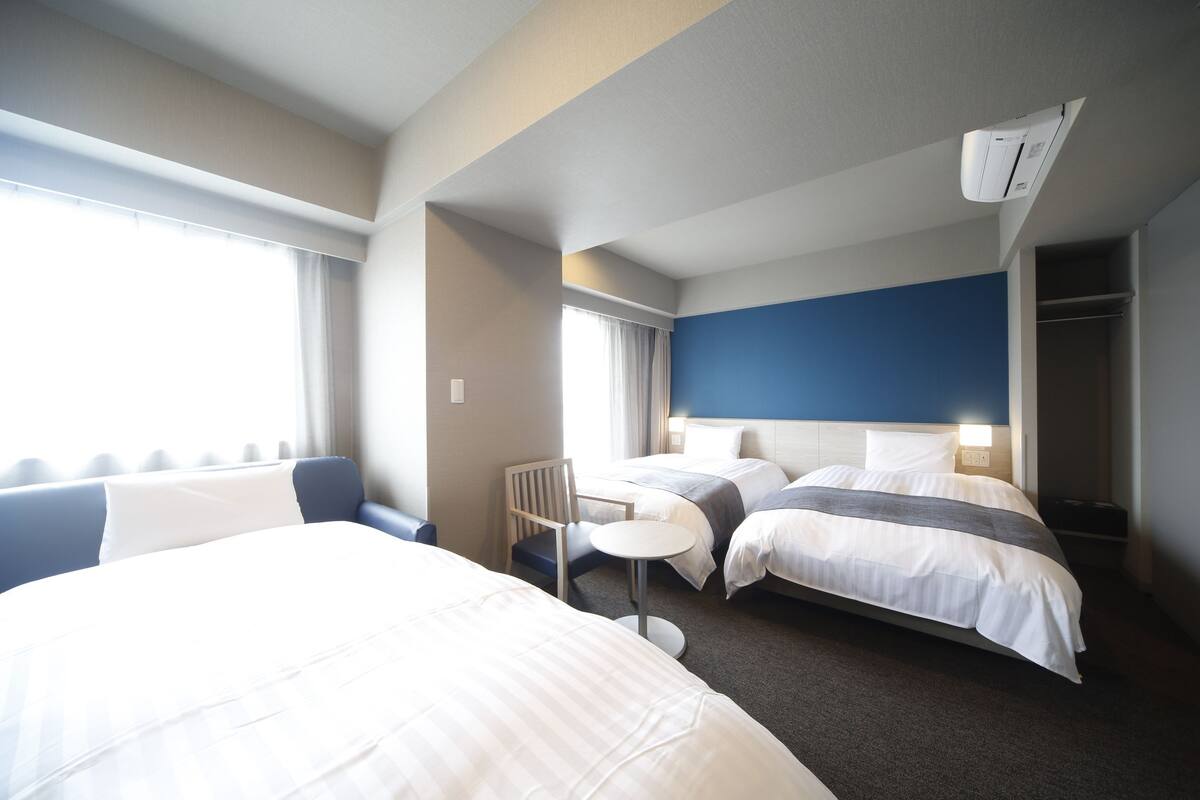 A hotel room with two beds, a small table, a chair, and a wardrobe.