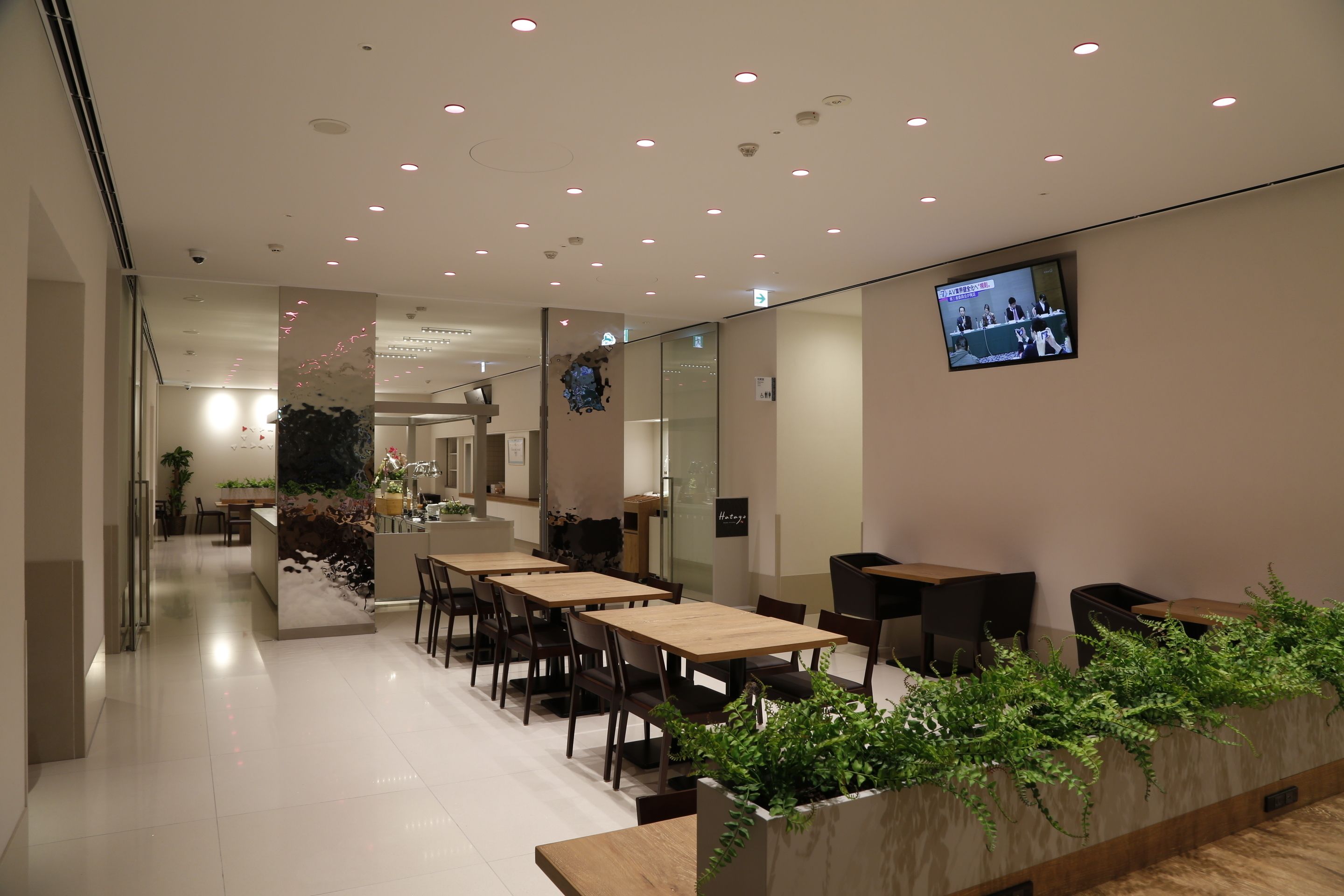 A modern dining area with tables and chairs, a television screen, and a plant wall.
